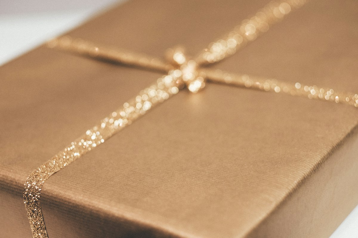 A gift box wrapped in gold-brown paper and tied with a glittering gold ribbon